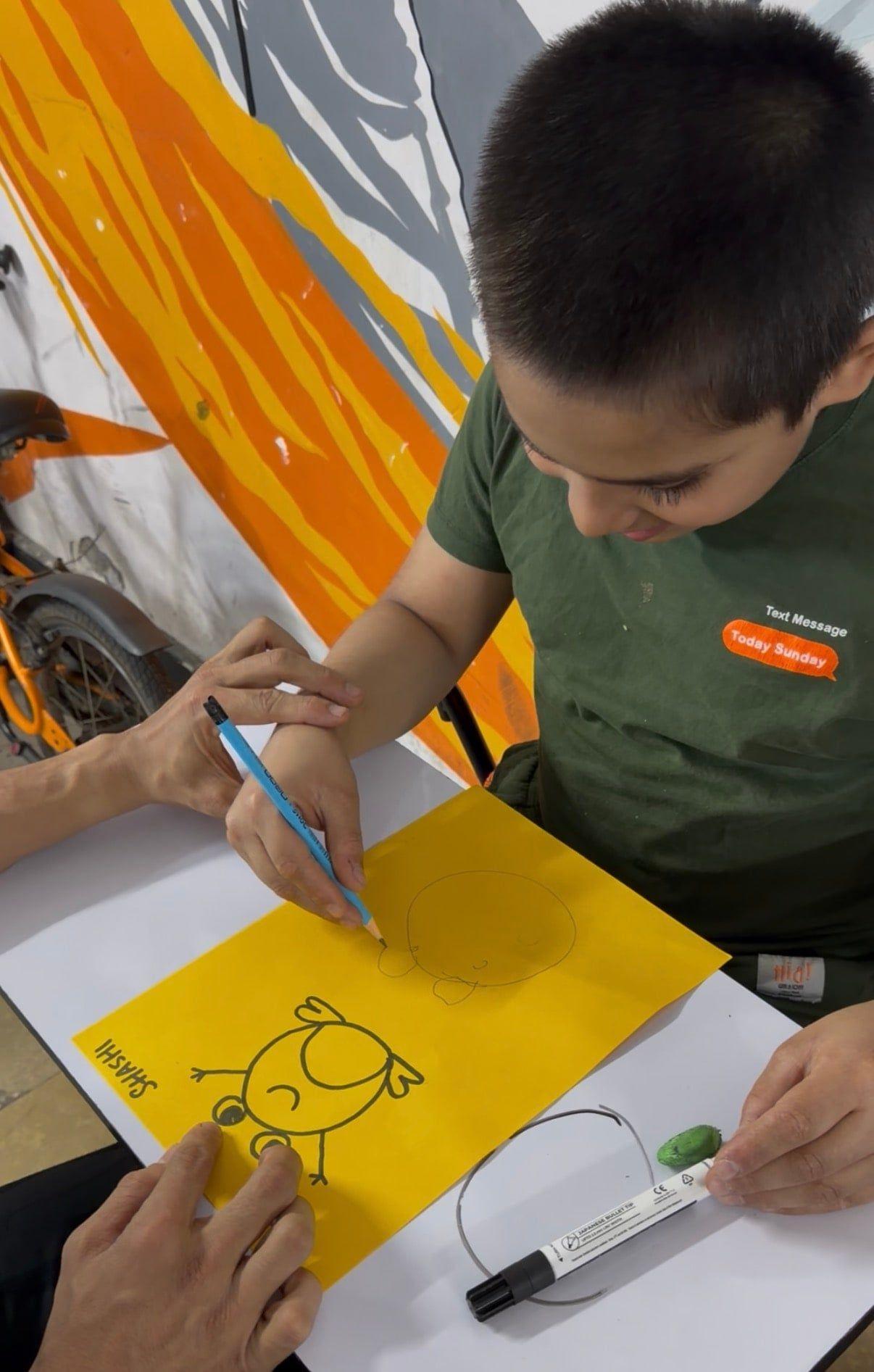 A child drawing while a coach guides their hand